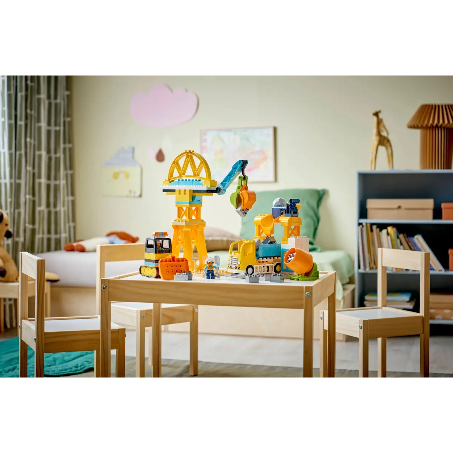Une chambre d'enfant avec un jeu de construction sur une table. Les jouets comprennent une grue, des camions et des figurines. Deux chaises.