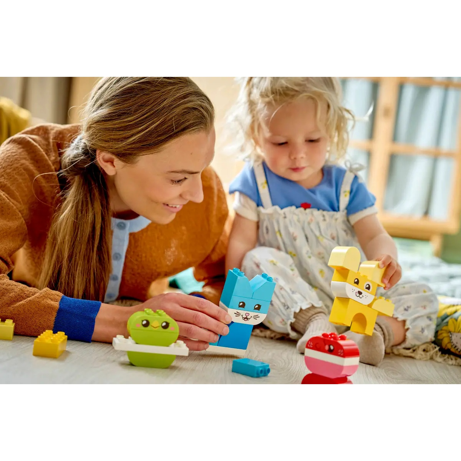 Une femme et un enfant jouent avec des blocs de jouets colorés en forme d'animaux. La scène se déroule à l'intérieur, sur un sol en bois.