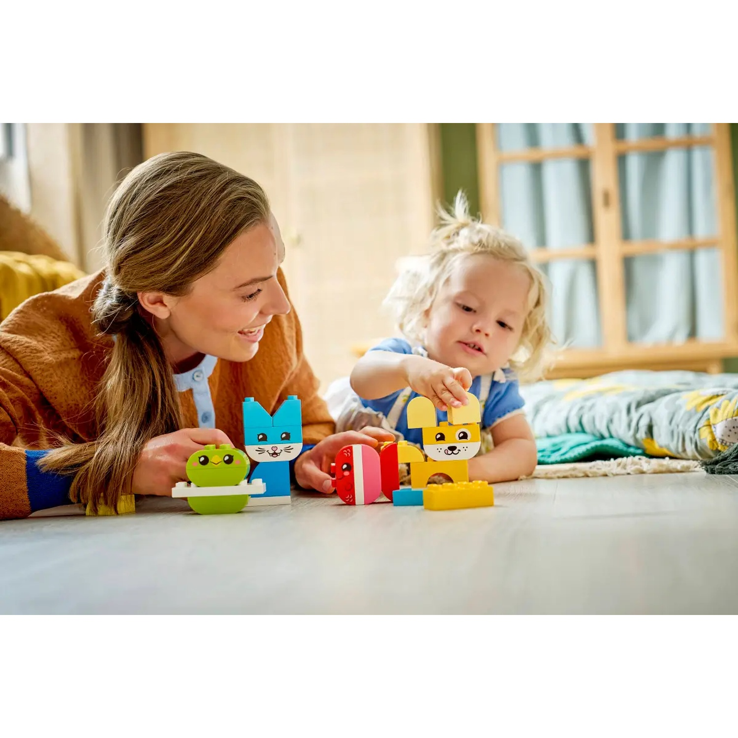 Une femme et un enfant jouent avec des blocs de construction colorés. Ils sont sur un sol en bois, souriants et concentrés sur les jouets.