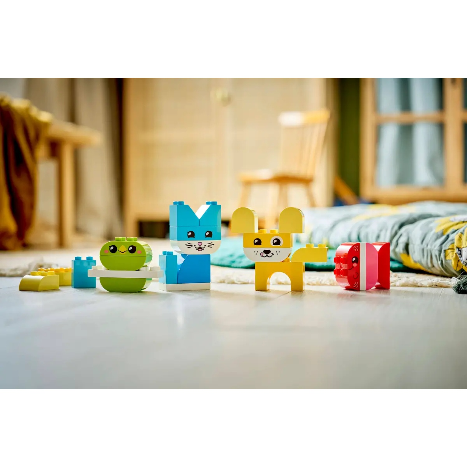 Des figurines d'animaux jouets colorées faites de blocs sont posées sur un sol en bois. Une grenouille, un lapin, un chien et une figurine rouge et blanche sont visibles.