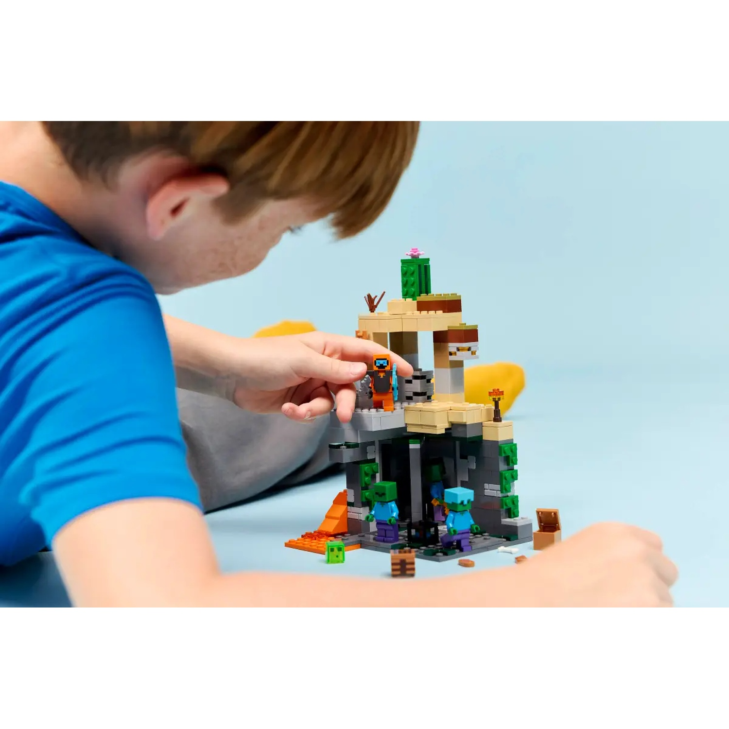 Un enfant joue avec un jeu Lego Minecraft. L'ensemble représente une grotte avec des zombies, un coffre et une figurine.