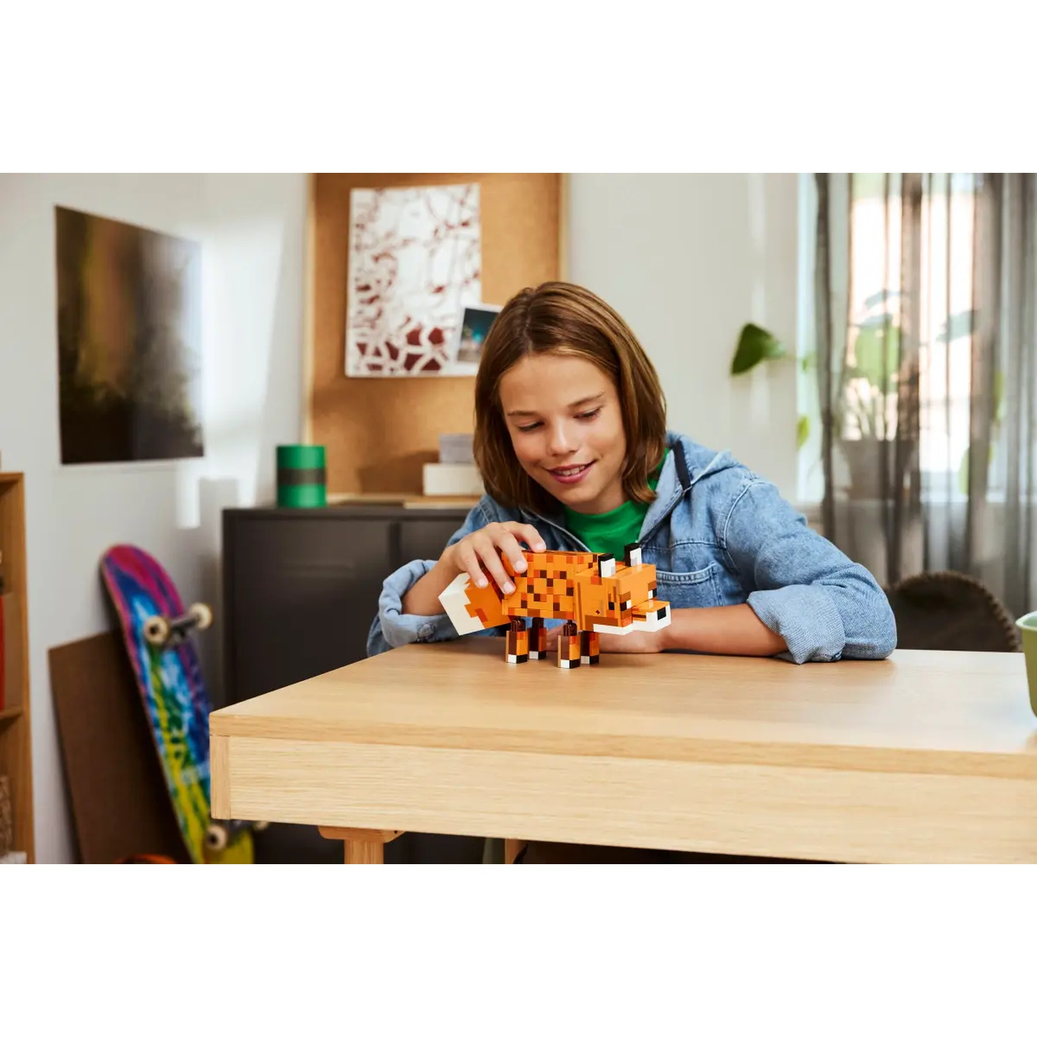 Un enfant sourit, tenant un renard Lego sur une table en bois. Un skateboard et une armoire noire en arrière-plan.