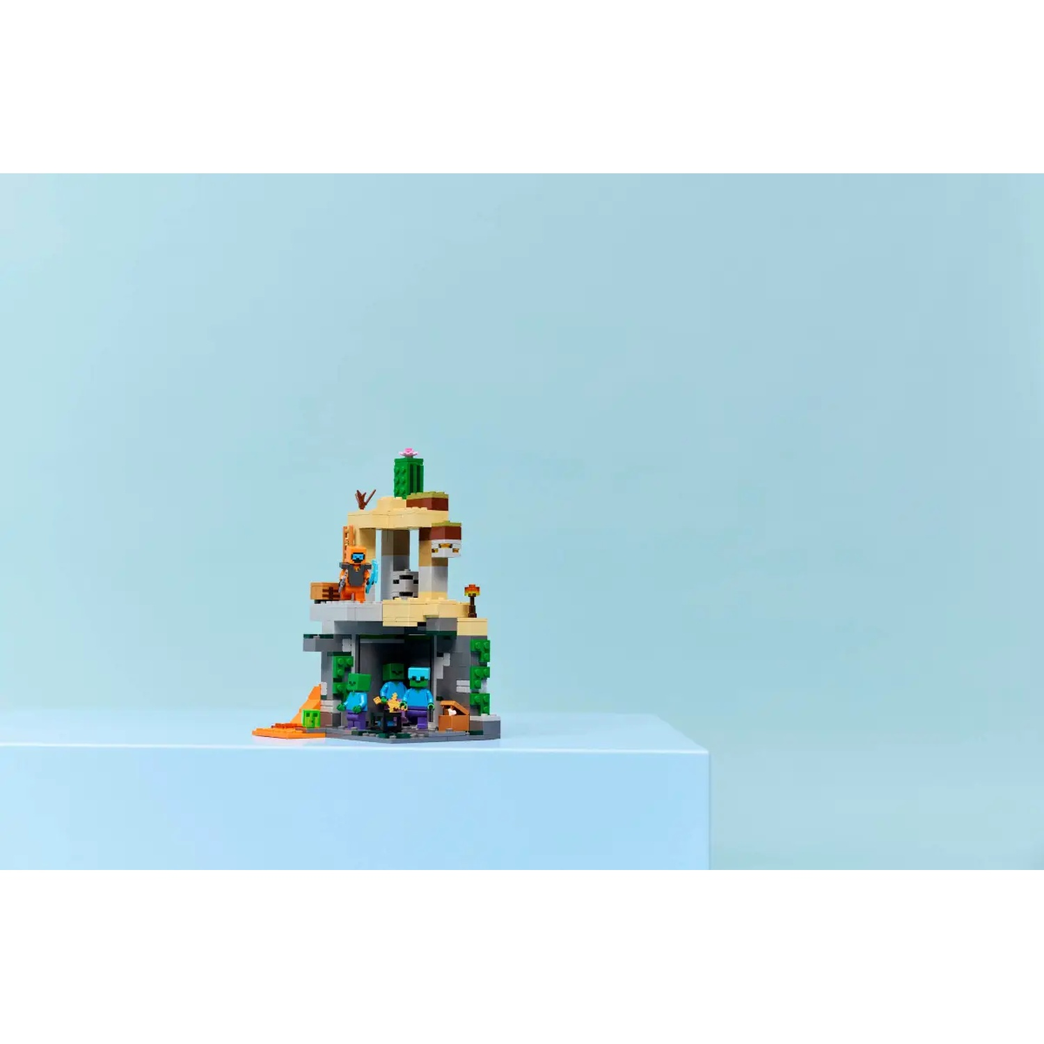 Un jeu Lego Minecraft sur une surface bleue. L'ensemble représente une scène de grotte avec des figurines et des blocs de différentes couleurs.