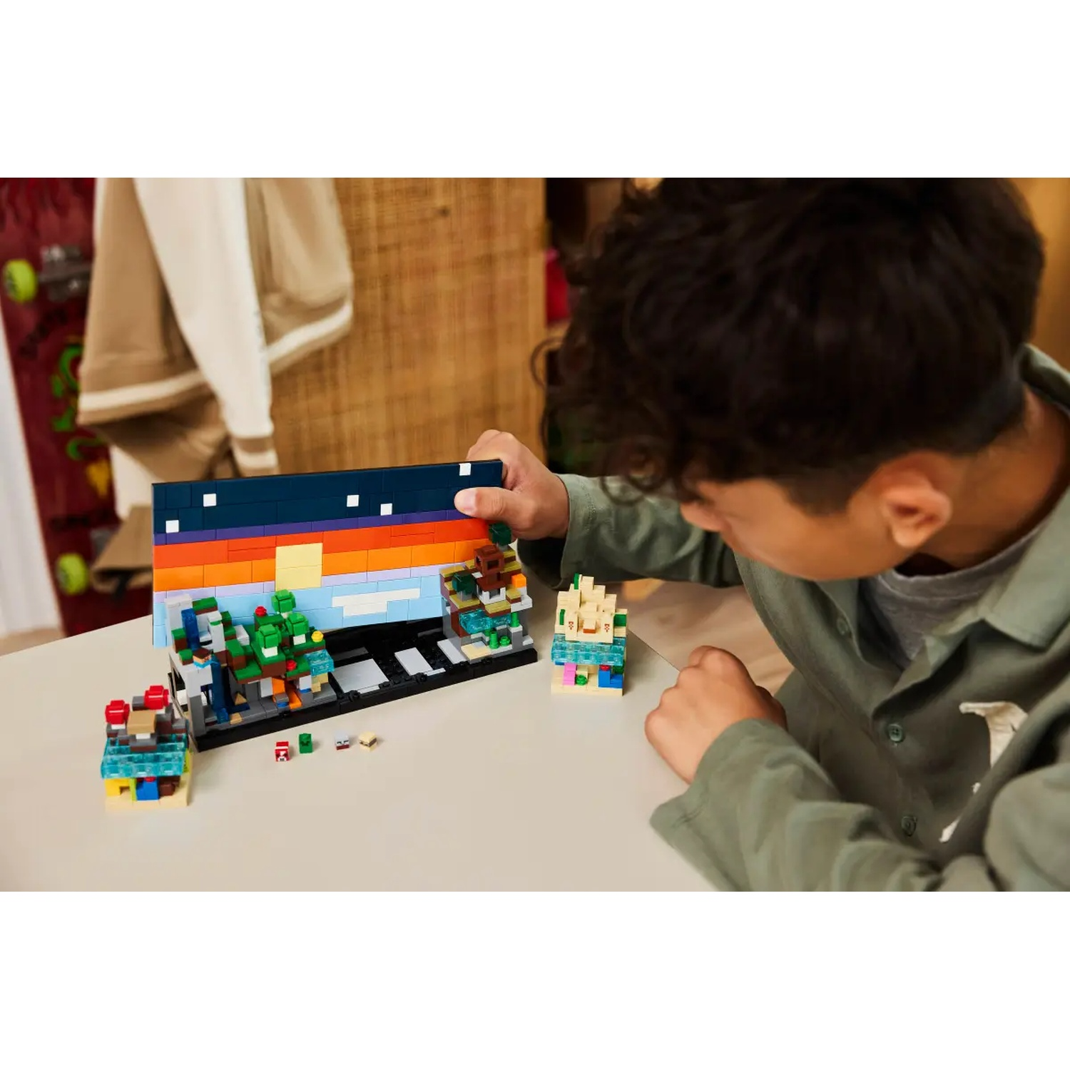 Une personne construit avec des briques Lego. L'ensemble Lego représente une scène colorée avec un ciel bleu foncé et divers bâtiments.