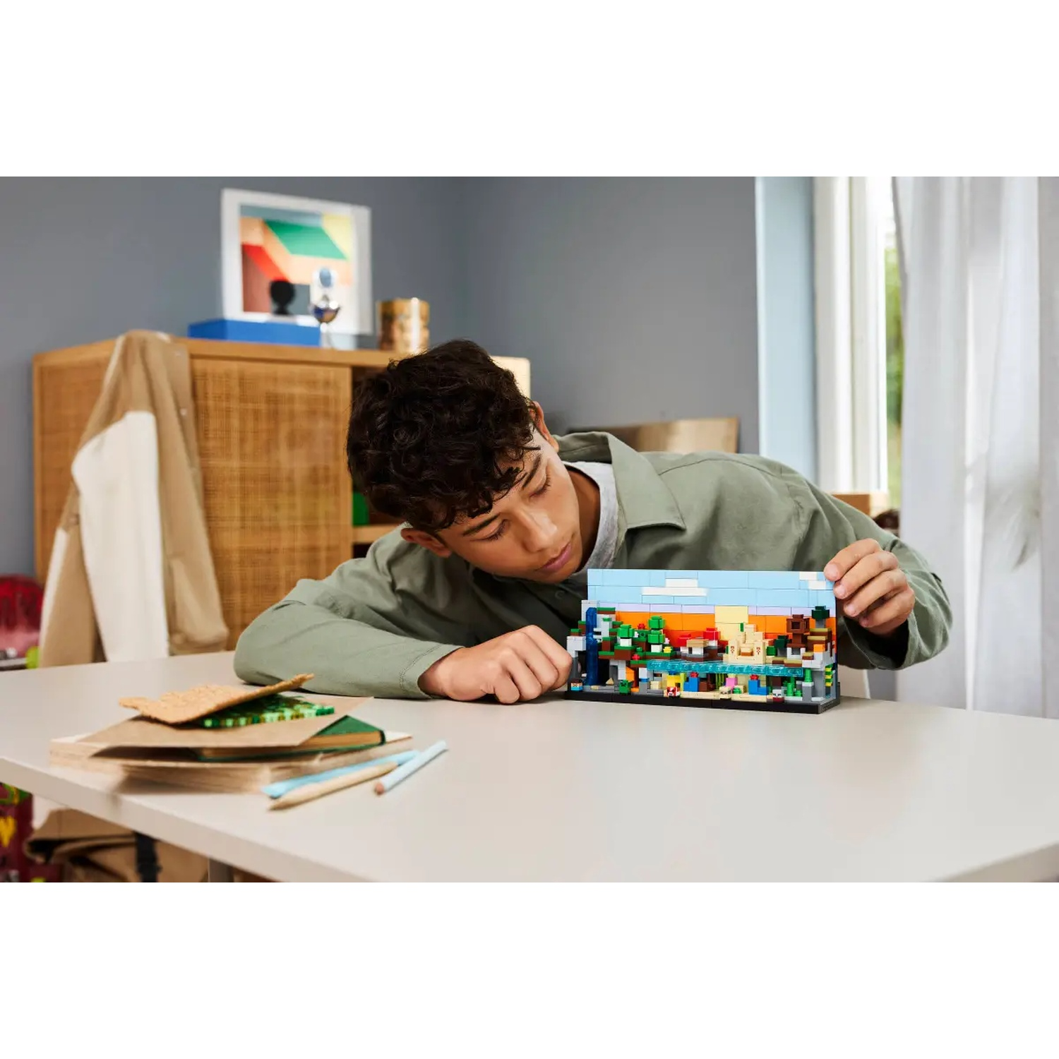 Une jeune personne se penche sur une table, examinant un diorama Lego. Le diorama représente un paysage coloré avec des bâtiments et des arbres.