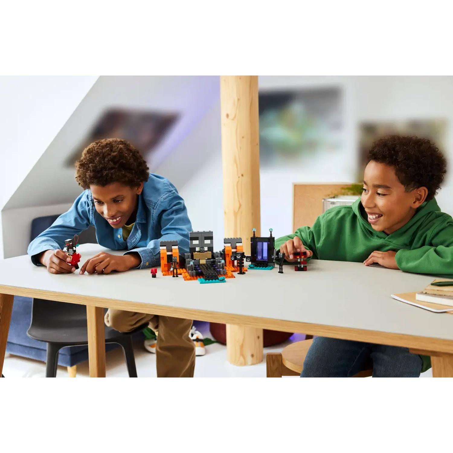 Deux garçons jouent avec des Lego sur une table. L'un porte une chemise bleue, l'autre un sweat à capuche vert. Des structures Lego sont sur la table.