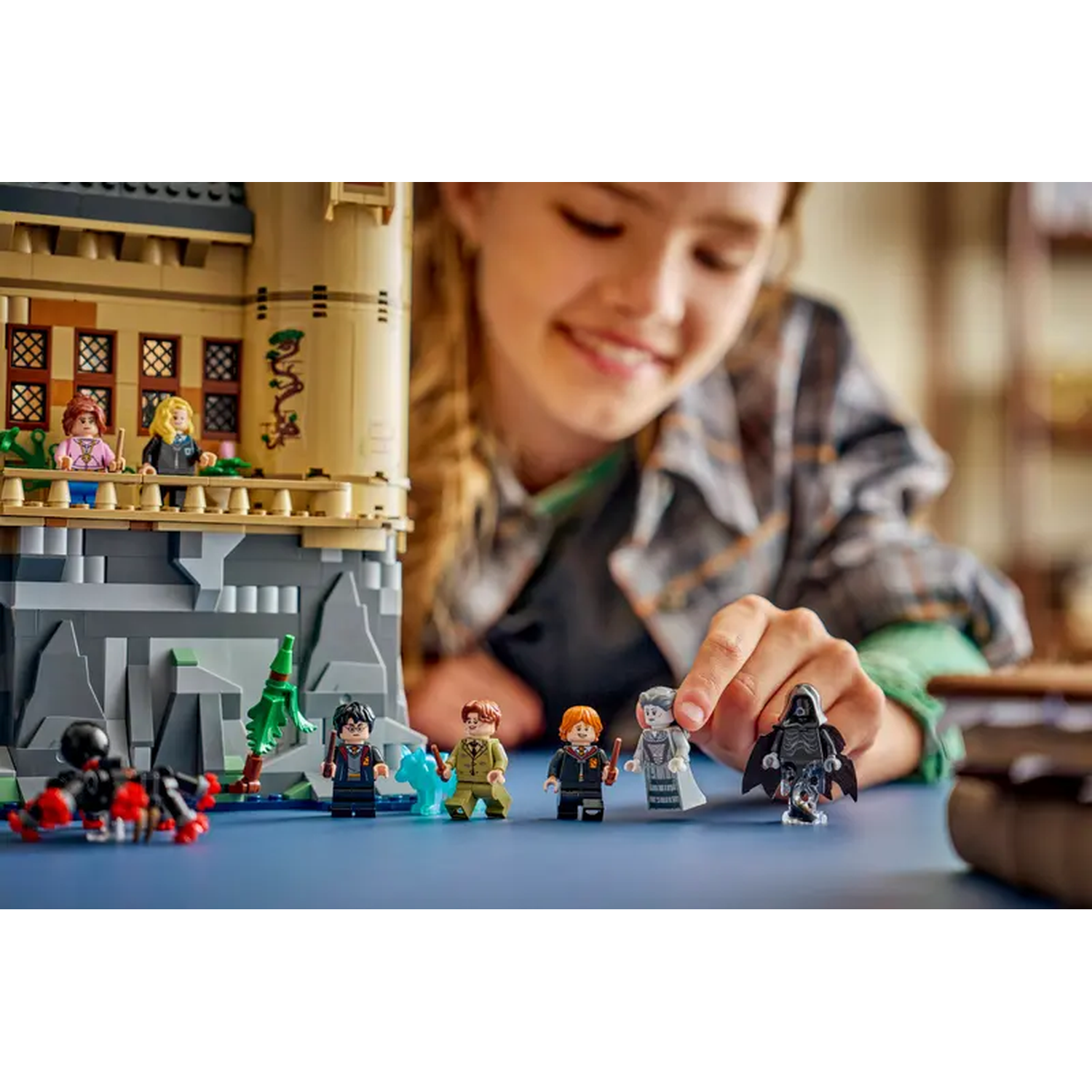 Een meisje speelt met Lego Harry Potter figuren. Een kasteel en enkele personages op de voorgrond, met een boek rechts.
