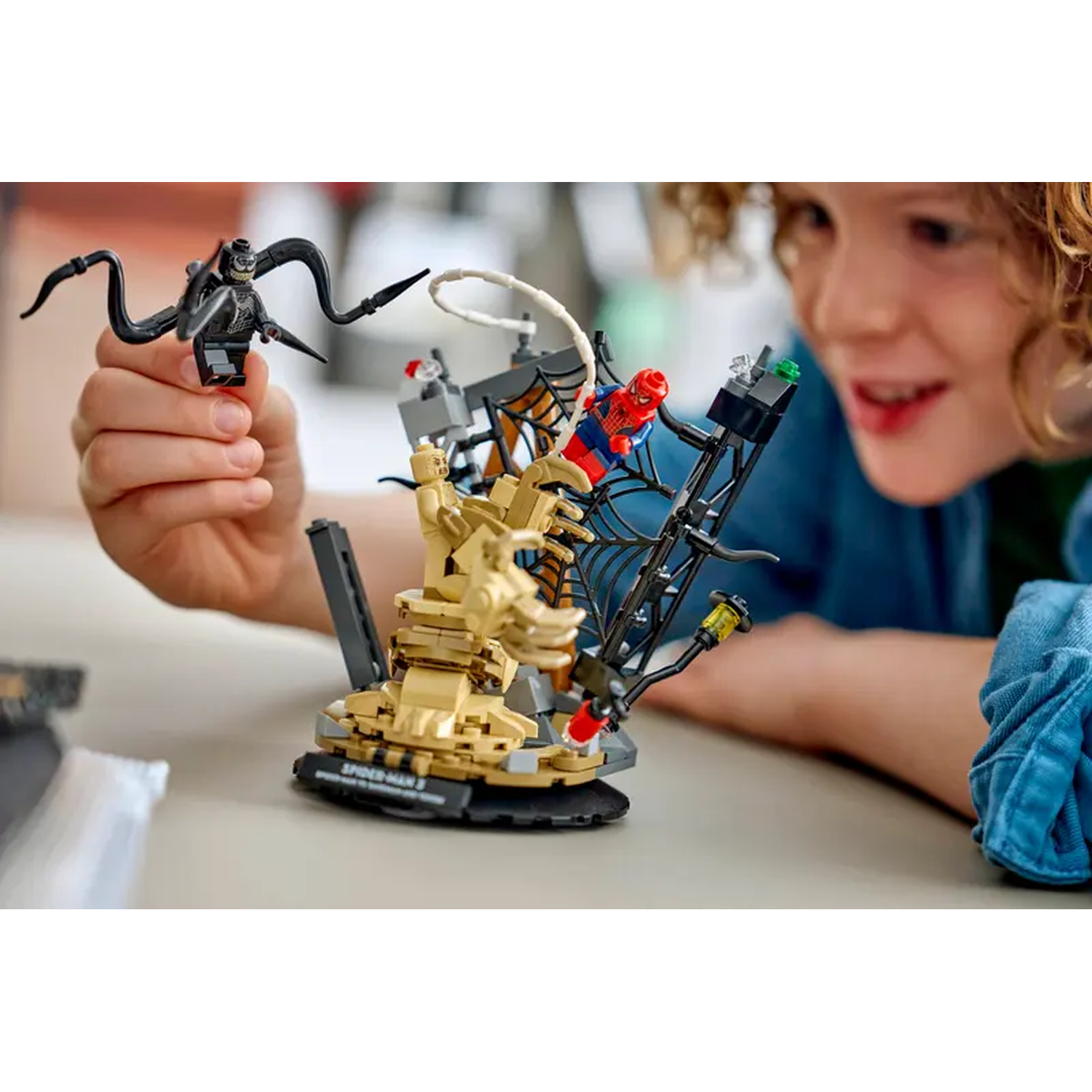 A child is holding a Lego figure. Lego set features Spider-Man and Venom. The child smiles, looking at the toy. 
