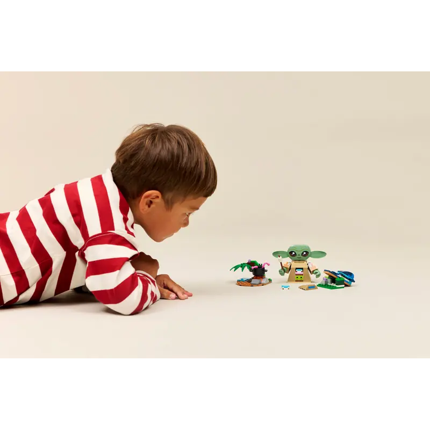 A child in a red and white striped shirt looks at a Lego set featuring a Grogu figure and other Lego pieces.