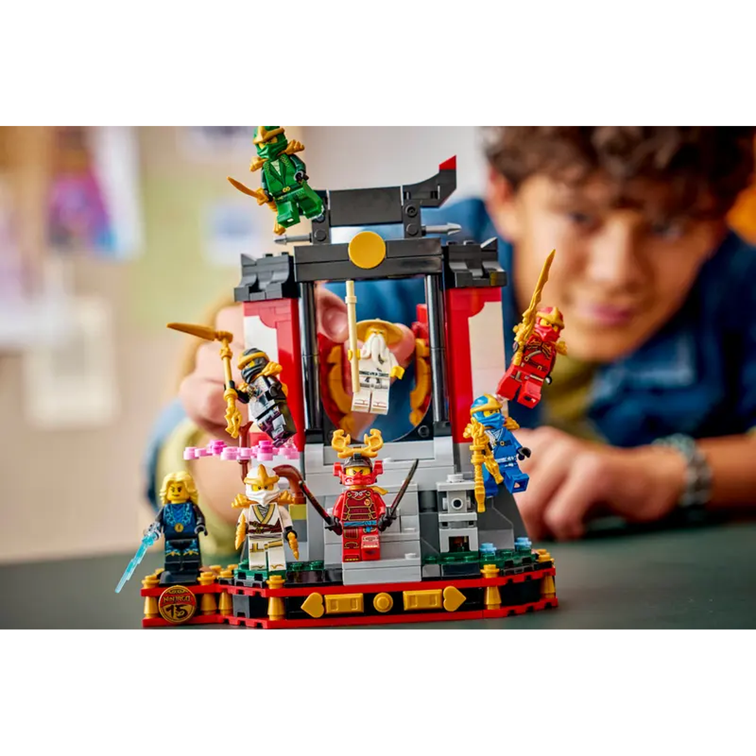 A person is playing with a Lego Ninjago set, featuring several colorful ninja figures and a temple-like structure.