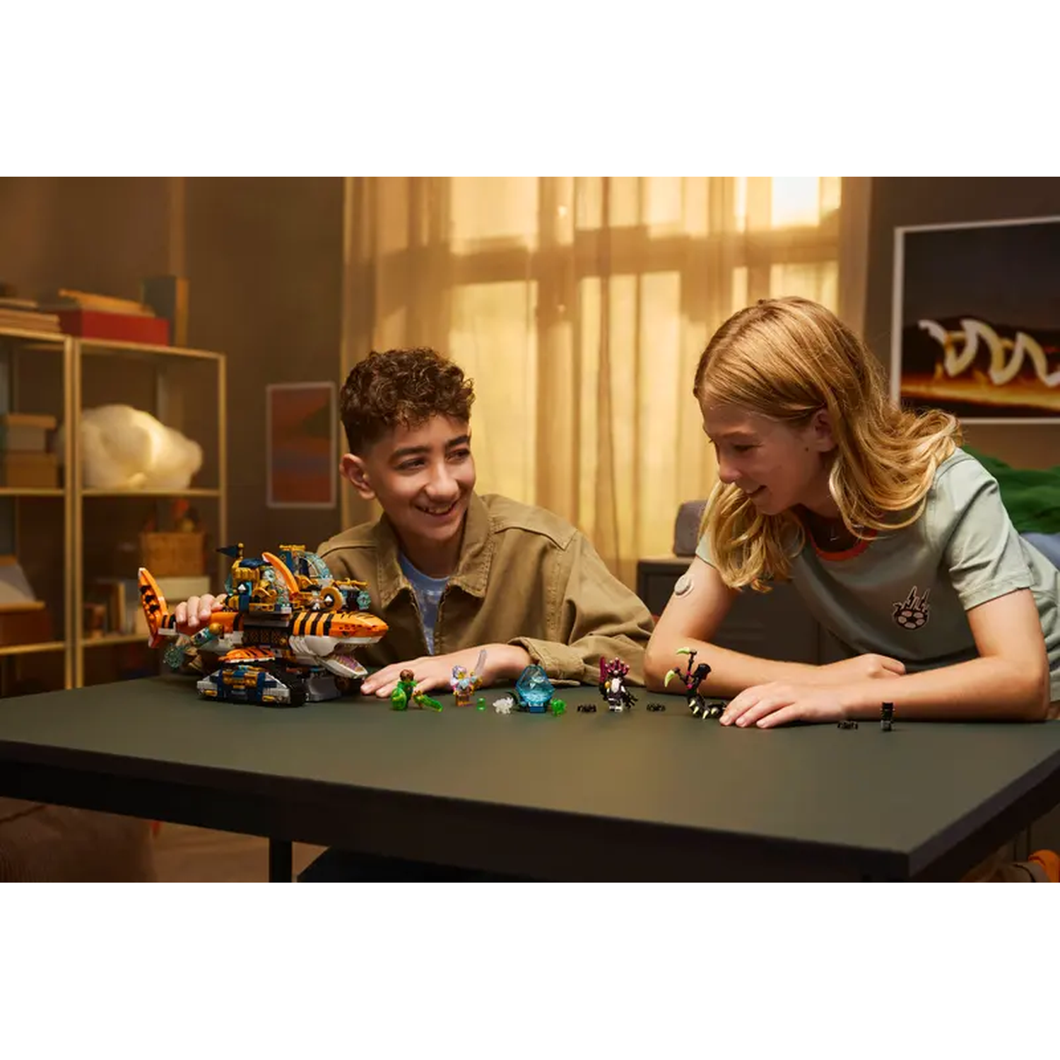 Twee kinderen spelen met een Lego set op een tafel. Eén lacht en kijkt naar een Lego voertuig. De ander heeft speelgoed.