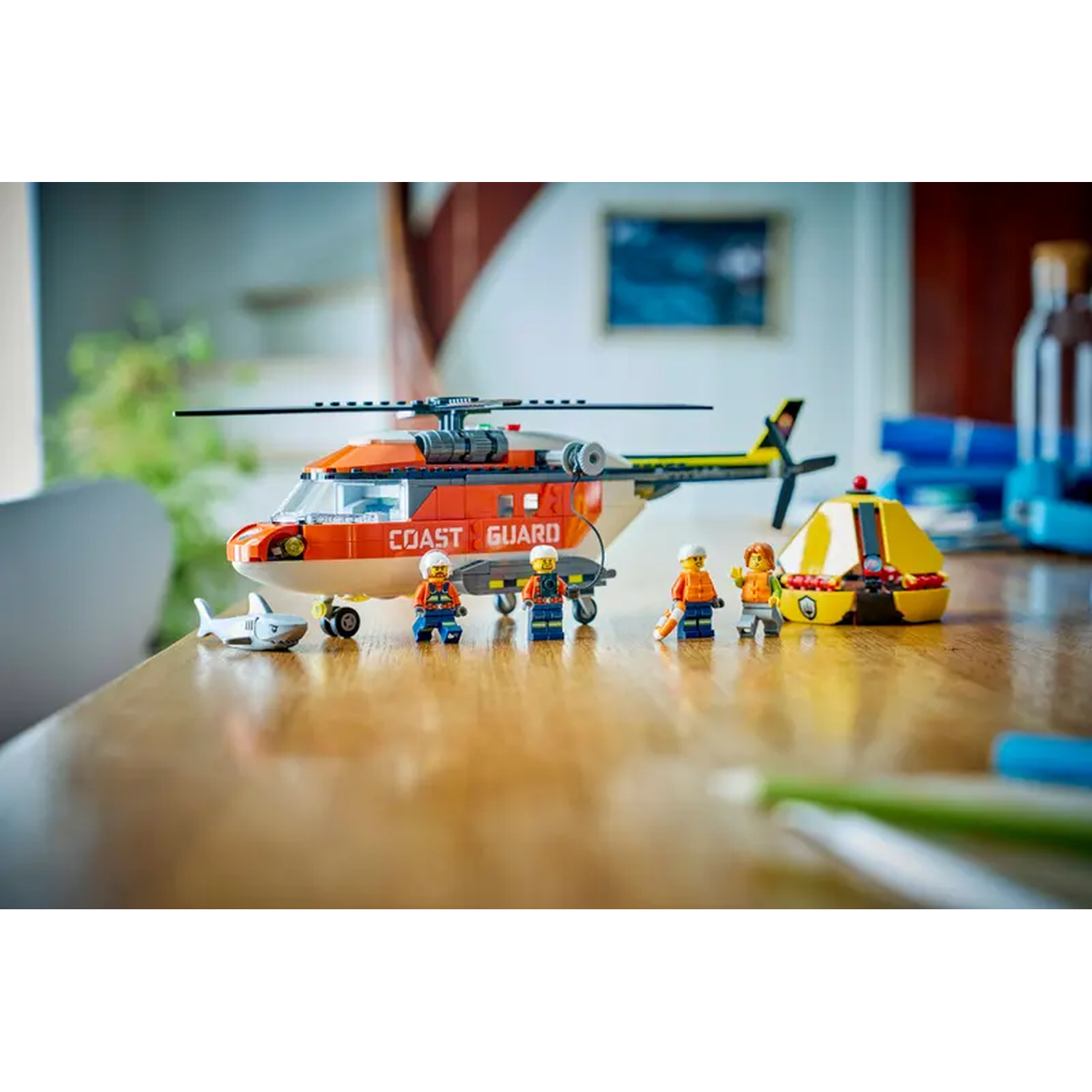 A Lego Coast Guard rescue scene. It features a helicopter, shark, several minifigures, and a yellow rescue boat, all on a wooden table.