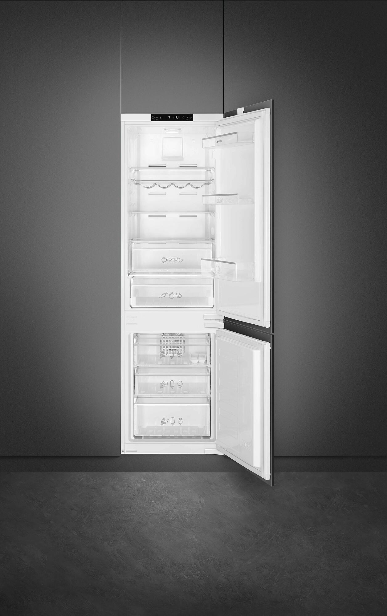 Offener weißer Kühlschrank mit Gegenständen im Inneren. Die Tür ist angelehnt. Er steht in einer grauen Wand und auf einem grauen Boden.