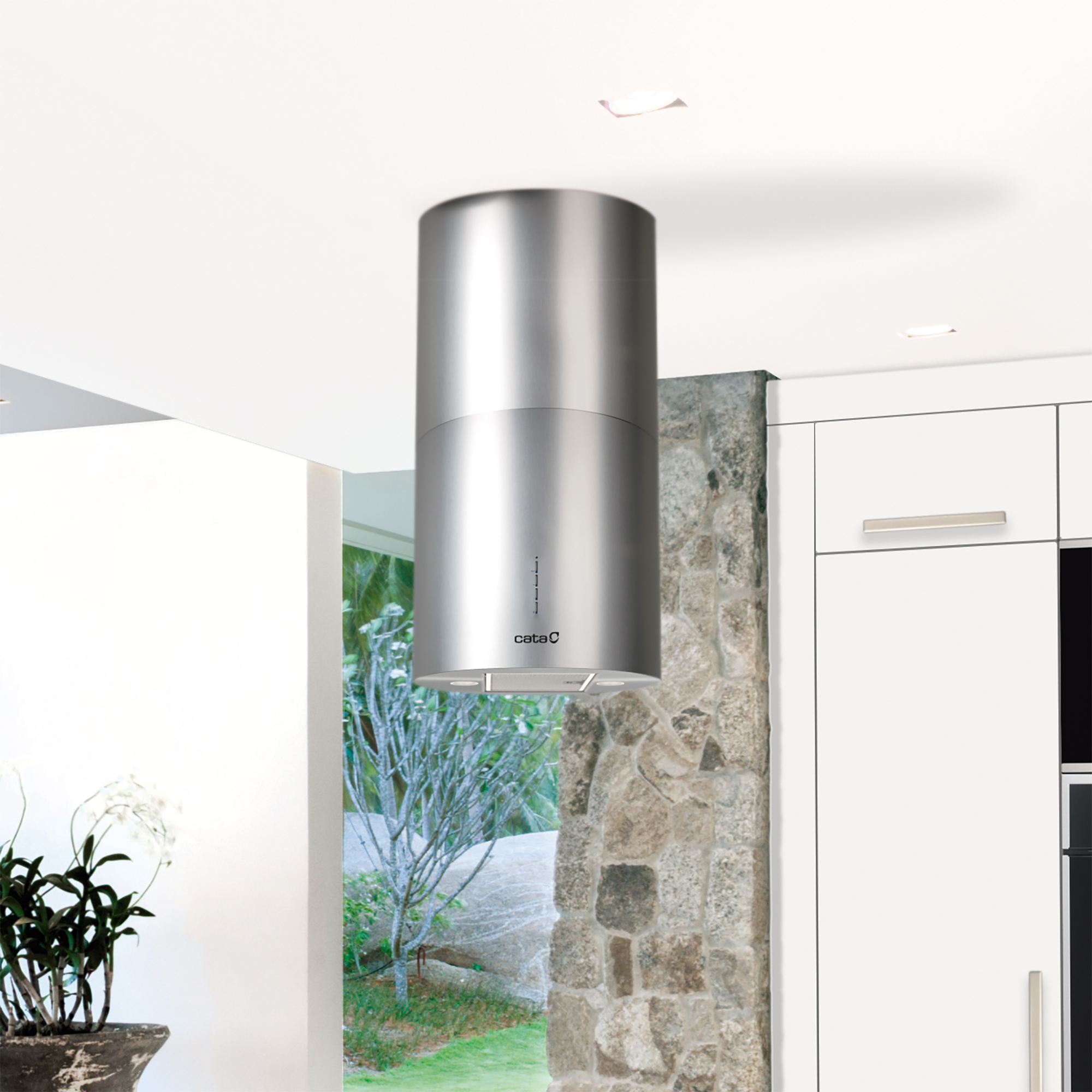 Una campana extractora cilíndrica de acero inoxidable cuelga del techo blanco. Se ve una pared de piedra y armarios blancos.