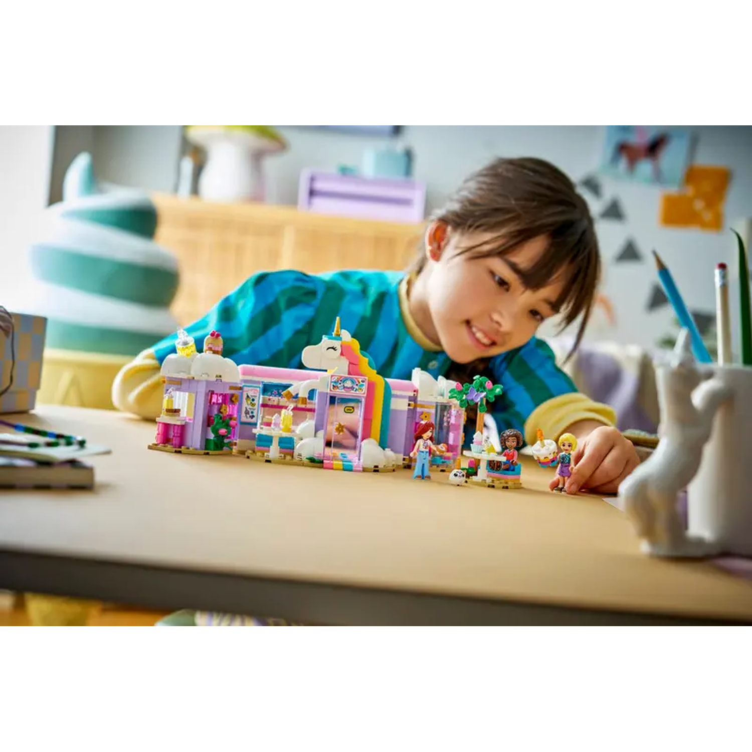 A girl looks at a Lego set. The set is a unicorn shop with mini figures. The set is on a table.