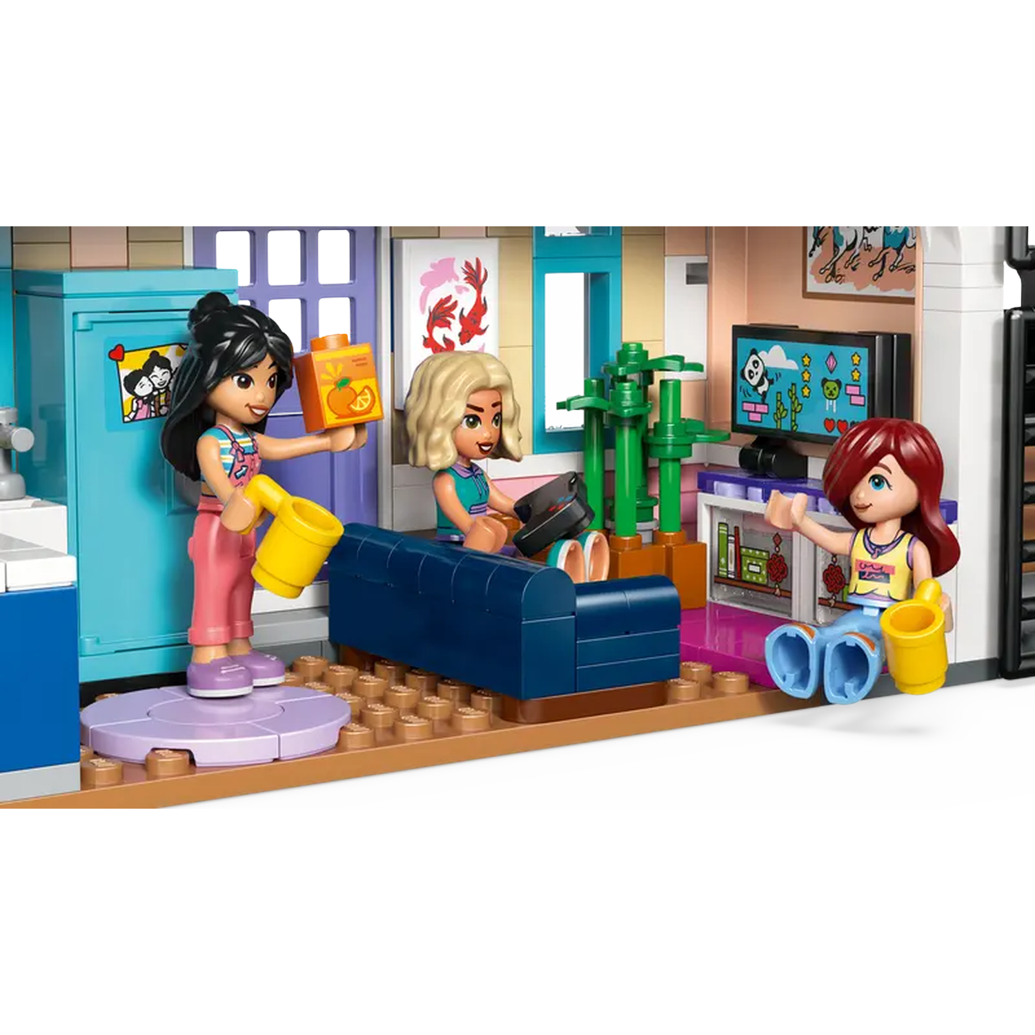 Lego scene of three girls in a room. One holds juice, another plays with a console, and the third sits. A TV and a cabinet are visible.