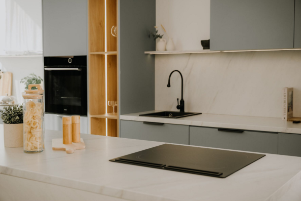 Nowoczesna kuchnia z czarną płytą grzewczą, zlewozmywakiem i kranem. Są drewniane szafki i marmurowy blat.