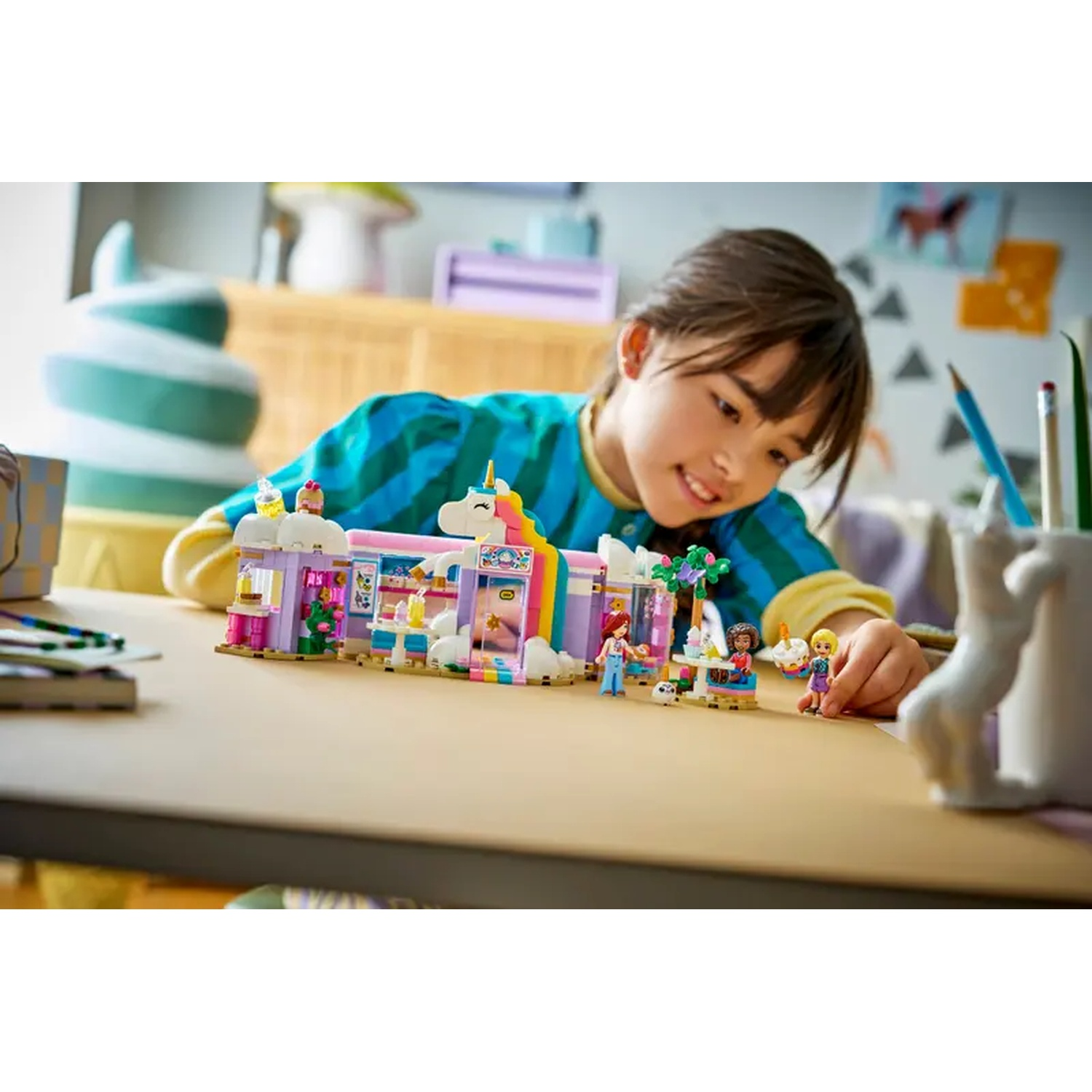 A girl looks at a Lego set. It has a unicorn theme. The set includes figures, a building, and a table.