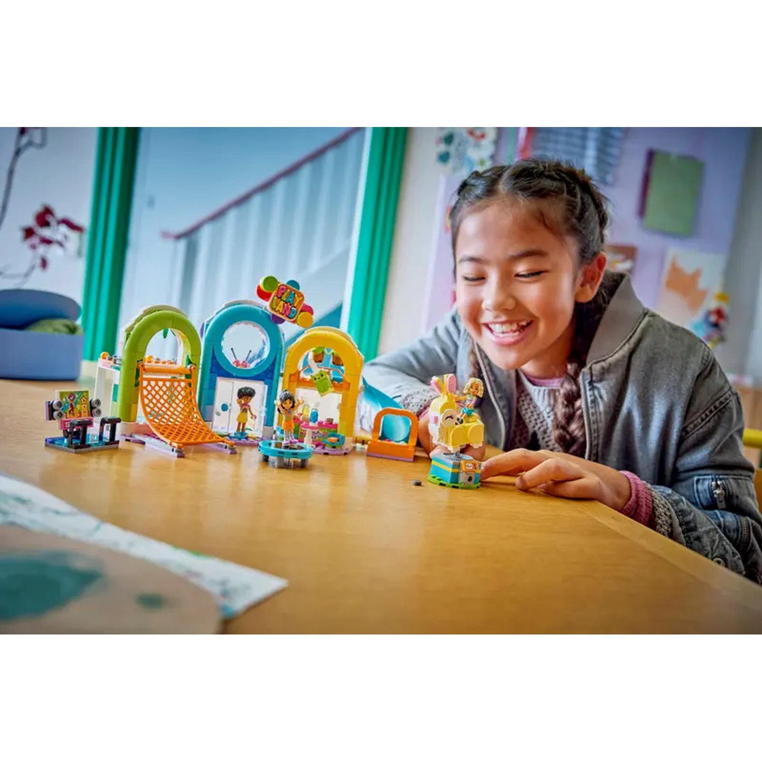 A smiling girl looks at a Lego set on a table. The set includes arches, figures, and an easter bunny structure.