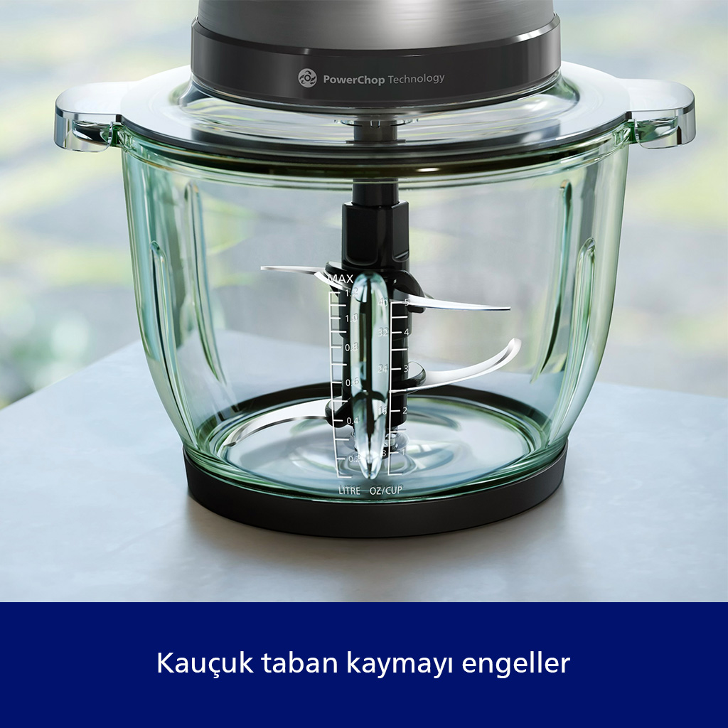 Cam kase, siyah bıçaklar ve gri bir üst kısmı olan bir mutfak robotu. Bulanık bir arka plan ile bir masanın üzerinde duruyor.