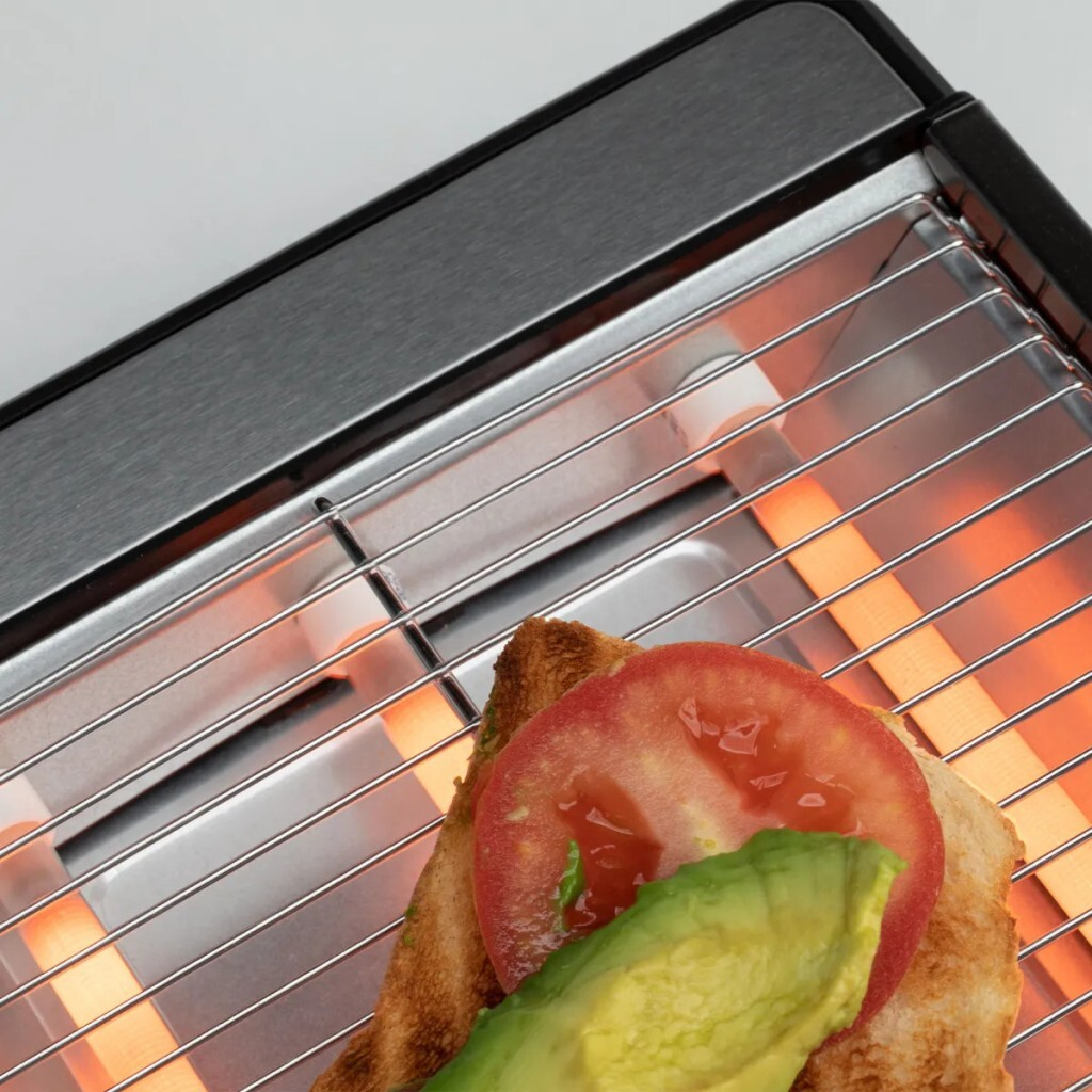 Una tostadora con una rebanada de pan cubierta con aguacate y tomate está dentro. Los elementos calefactores brillan en naranja.