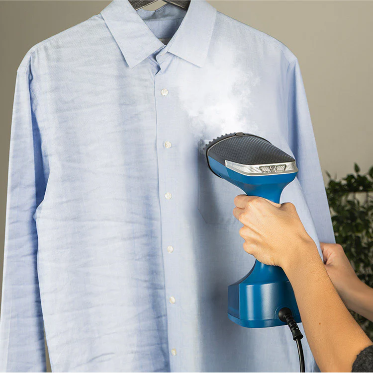 Una persona plancha una camisa azul claro con un vaporizador azul. La camisa cuelga de una percha. El vapor sale del vaporizador.