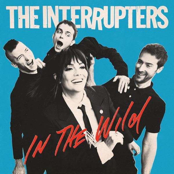 Die Bandmitglieder von The Interrupters posieren, lächeln. Text 'In The Wild' und Bandname auf blauem Hintergrund.