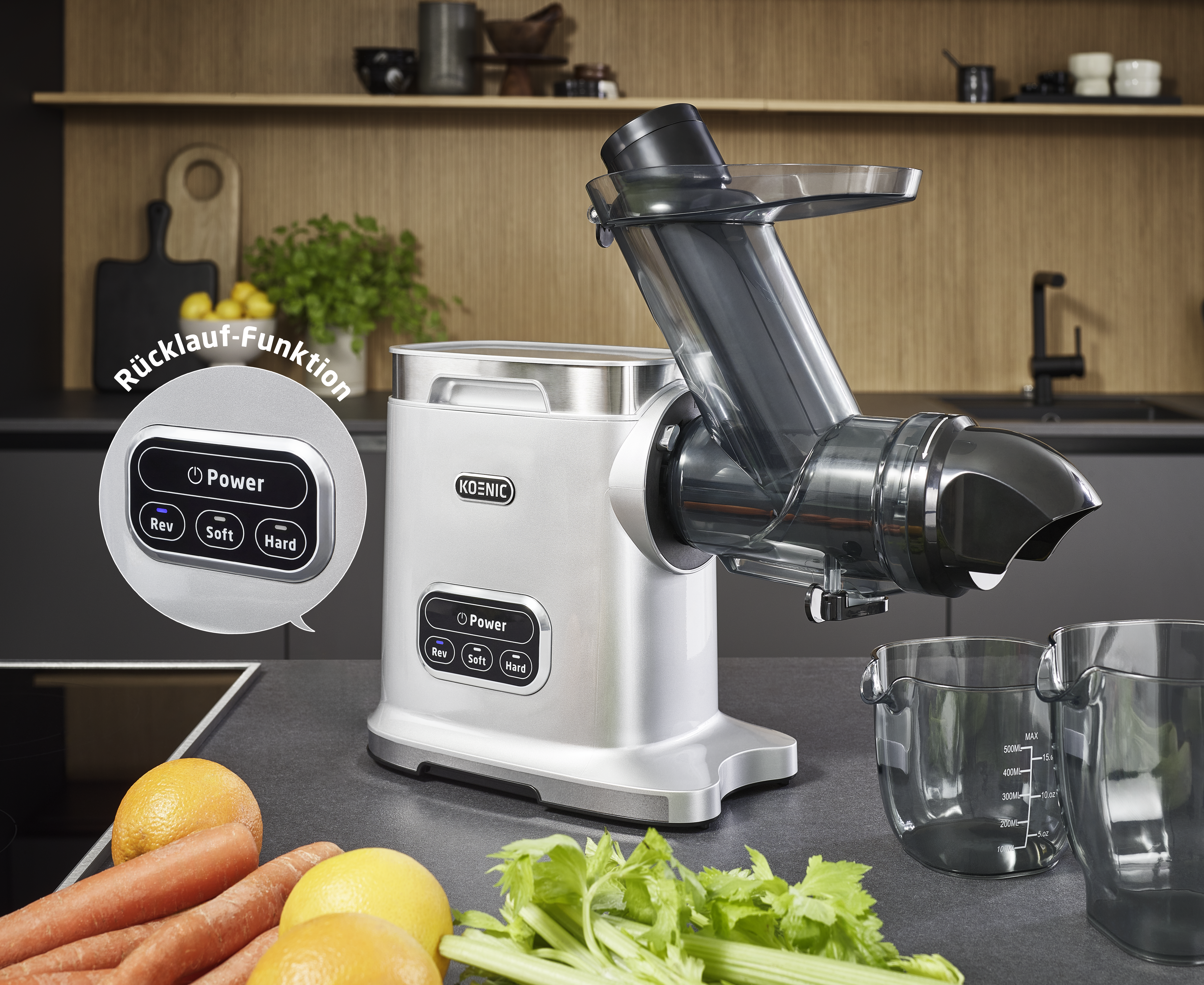 Srebrna wyciskarka stoi na blacie z pomarańczami, marchewkami i selerem.