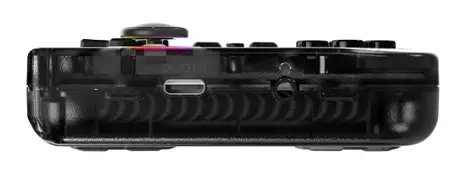 Widok z boku czarnego, przezroczystego kontrolera do gier. Posiada przyciski, joystick, porty do ładowania i słuchawek. Na białym tle.