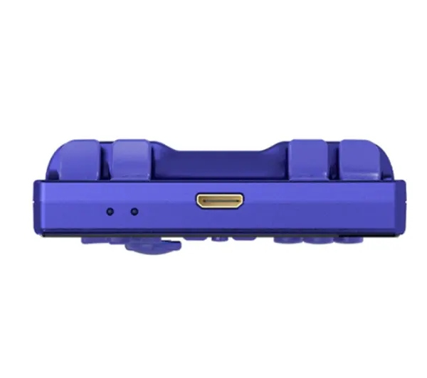 Fioletowe urządzenie do gier przenośnych. Posiada port USB, dwa małe otwory i podniesione przyciski. Białe tło.