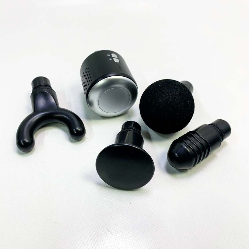 Czarny pistolet do masażu z nasadkami na białej powierzchni. Zawiera okrągłą, płaską i widlastą głowicę.