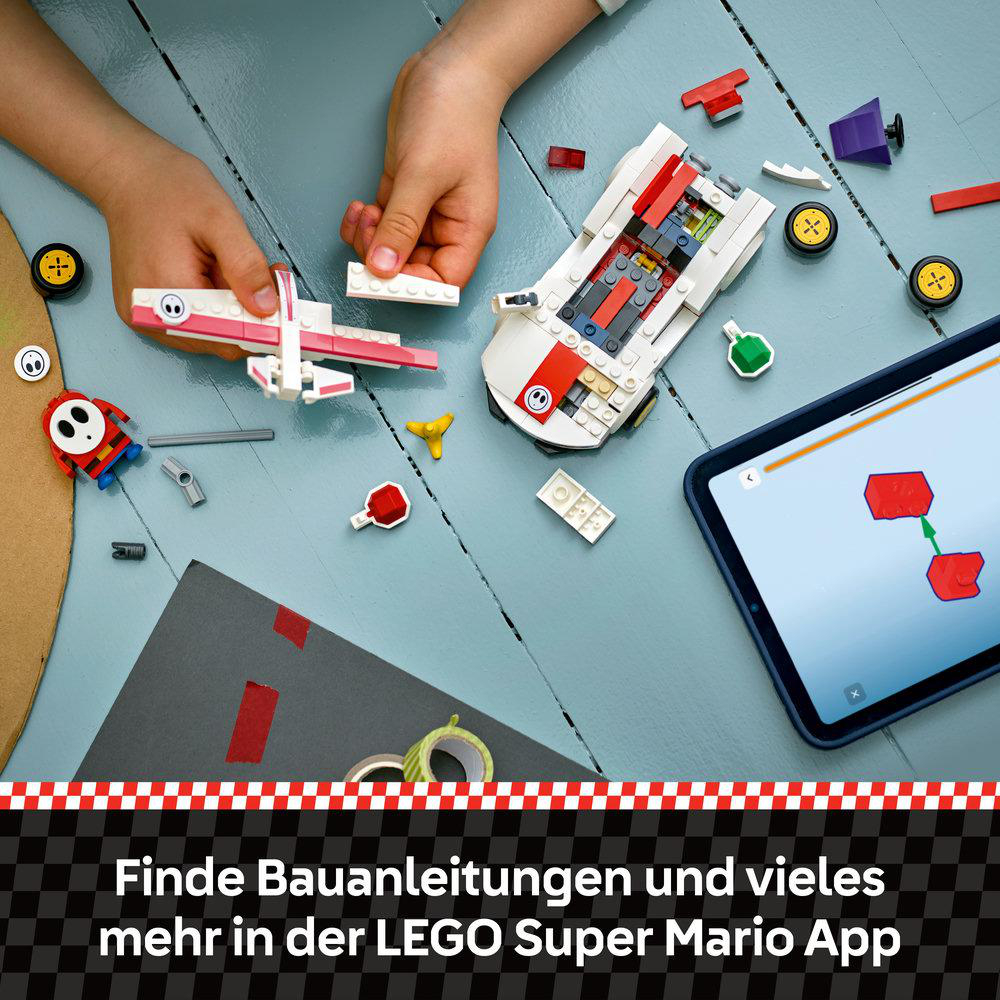 Hände bauen LEGO-Spielzeug zusammen. Teile eines Flugzeugs und eines Autos sind sichtbar, zusammen mit einem Tablet.