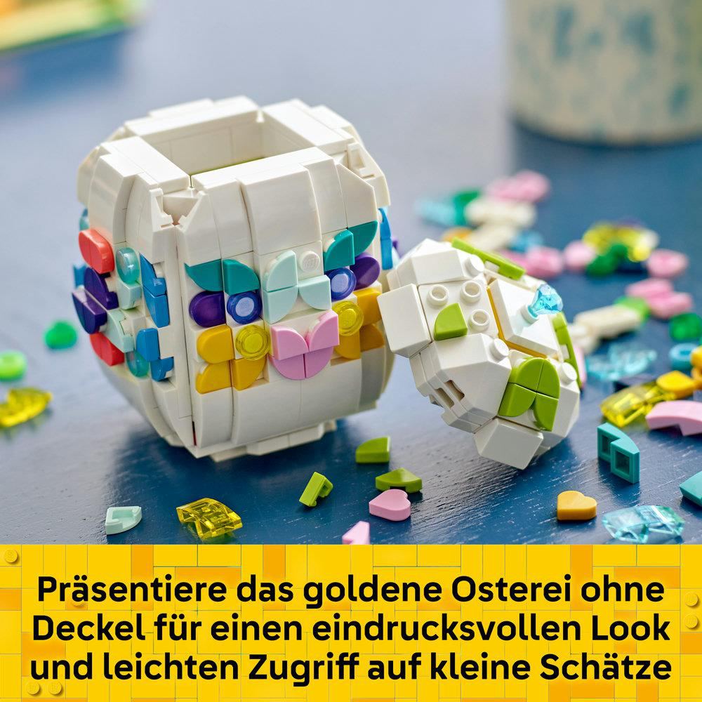 Weißes Lego-Osterei mit bunten Verzierungen, Deckel ab, auf blauer Oberfläche, umgeben von kleinen Lego-Teilen.