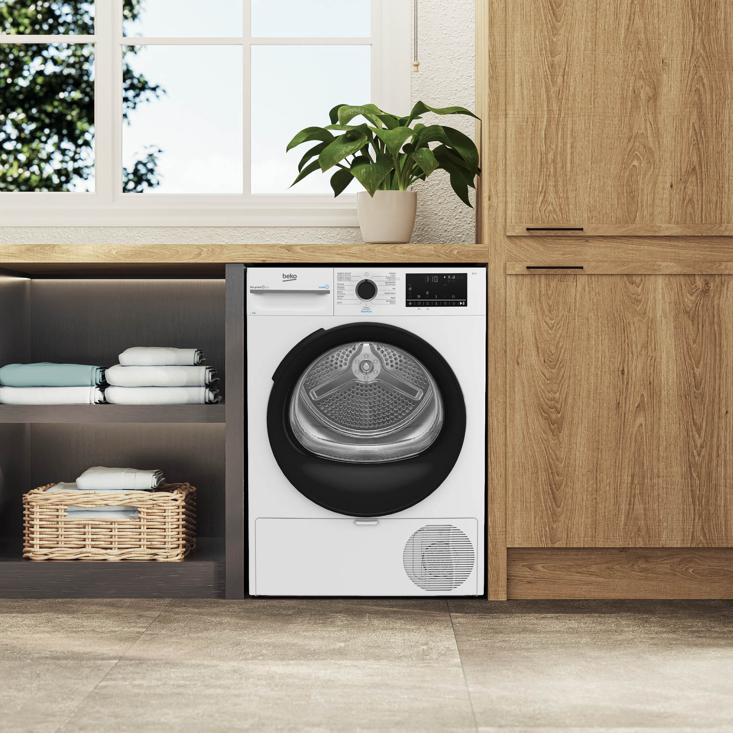 A white dryer stands between a wooden cabinet and a shelf with towels and a basket. A plant sits atop the dryer.