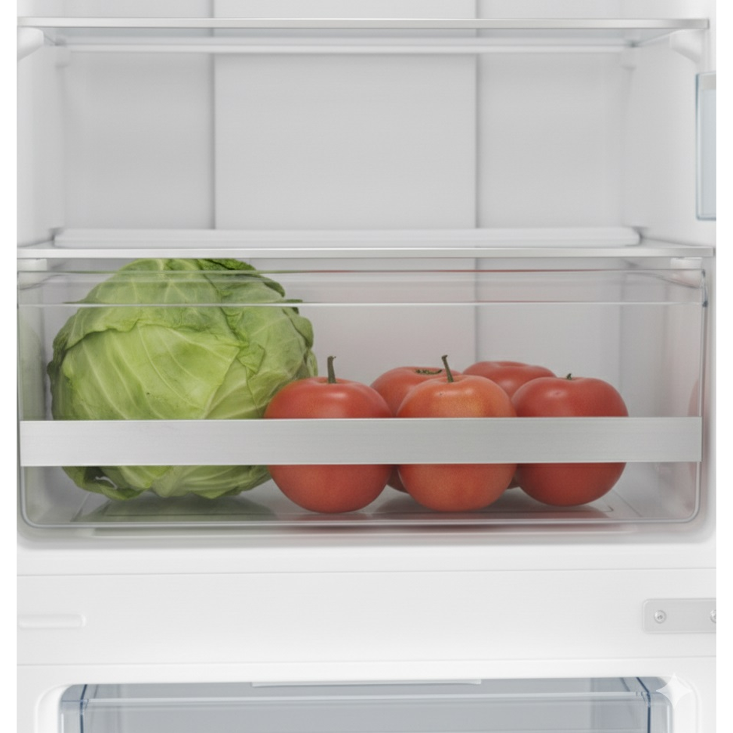 Inside a refrigerator: a cabbage and red tomatoes are visible in a clear drawer. The fridge interior is white.