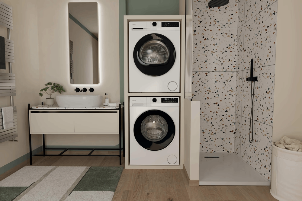 Escena de baño: dos lavadoras blancas apiladas, espejo, lavabo, ducha y pared de azulejos estampados.