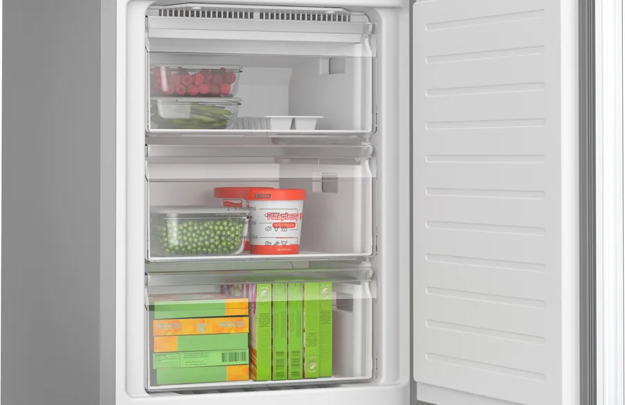 Congelador abierto con frambuesas, guisantes, espárragos, helado y cajas de alimentos congelados. Interior blanco con cajones transparentes.