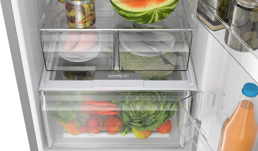 Refrigerador abierto lleno de frutas y verduras. Se ven sandía, lechuga, zanahorias, manzanas y rábanos.