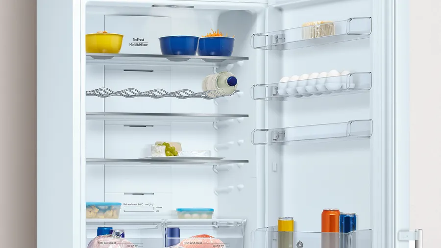 Refrigerador abierto lleno de comida: cuencos, huevos, queso, bebidas. Estantes con alimentos, una botella de agua y latas.