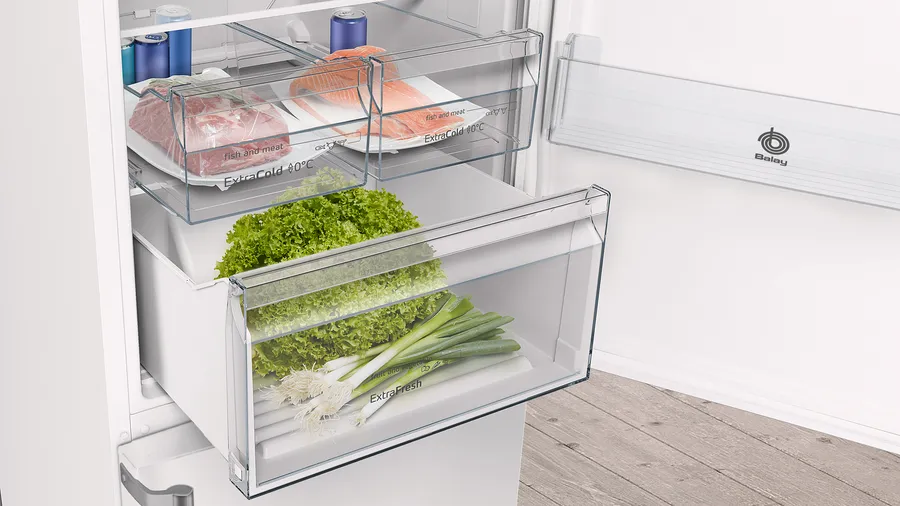 Refrigerador abierto con varios alimentos. Lechuga, cebolletas, carne y pescado son visibles dentro de los cajones del refrigerador.