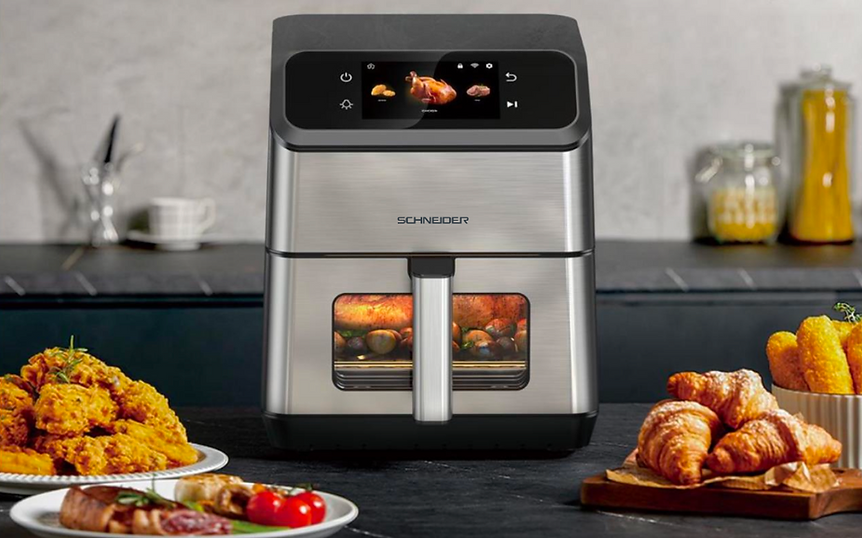 Une friteuse à air avec de la nourriture à l'intérieur, entourée d'aliments cuits comme du poulet frit, des croissants et d'autres plats.