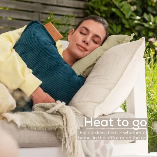 Una donna dorme all'aperto su cuscini con una coperta. Tiene un cuscino turchese con un oggetto marrone.