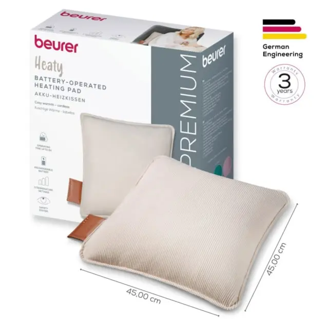 Un cuscinetto riscaldante beige con cinturini in pelle marrone è di fronte a una scatola del prodotto con il marchio 'beurer'.