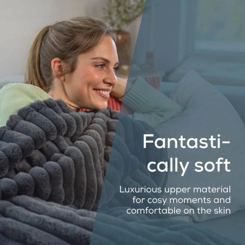 Donna sorride, avvolta in una coperta grigia e soffice. Testo: Fantasticamente morbido, materiale superiore lussuoso per momenti accoglienti.