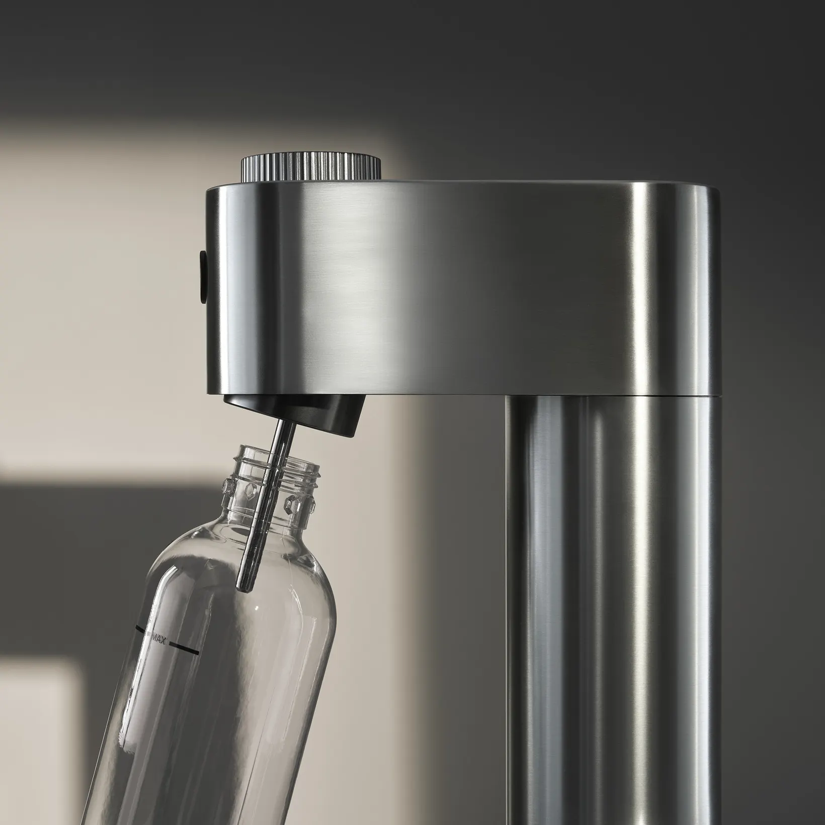 Un appareil à soda en acier inoxydable avec une bouteille en verre. La bouteille se remplit, avec une marque MAX.