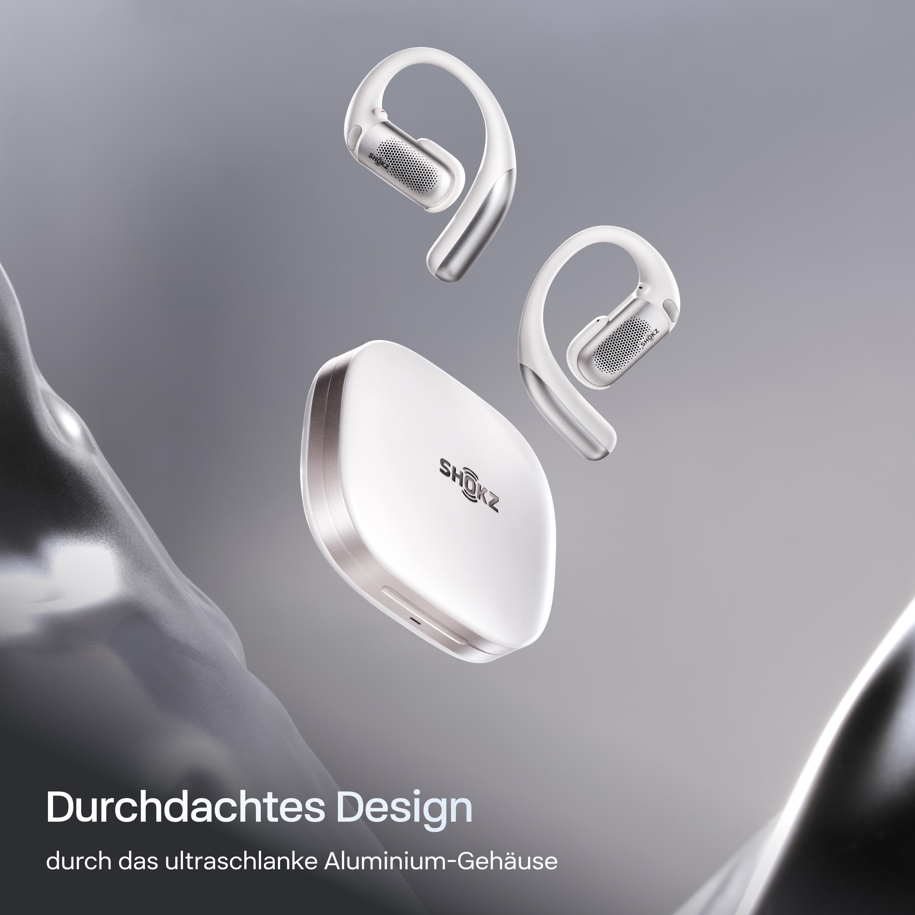 Weiße Shokz-Kopfhörer und -Hülle schweben vor grauem Hintergrund. Designt Text befindet sich unten im Bild.