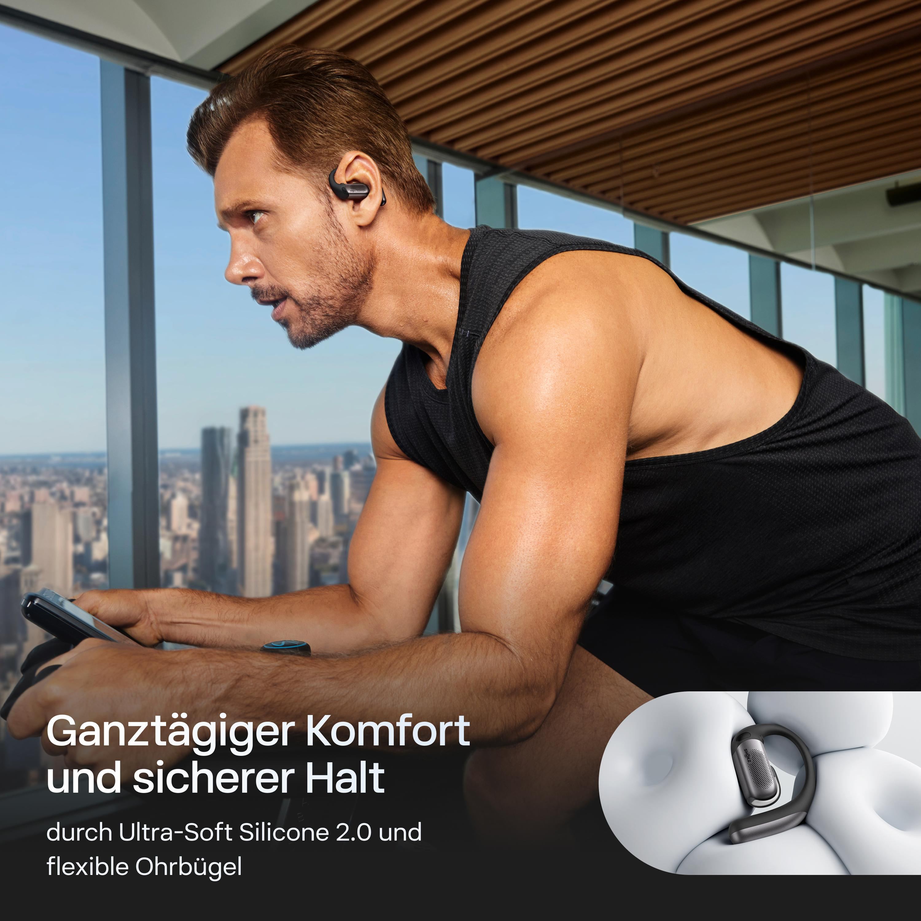 Ein Mann mit Kopfhörern trainiert. Er sitzt auf einem Heimtrainer. Im Hintergrund ist eine Stadtlandschaft zu sehen.