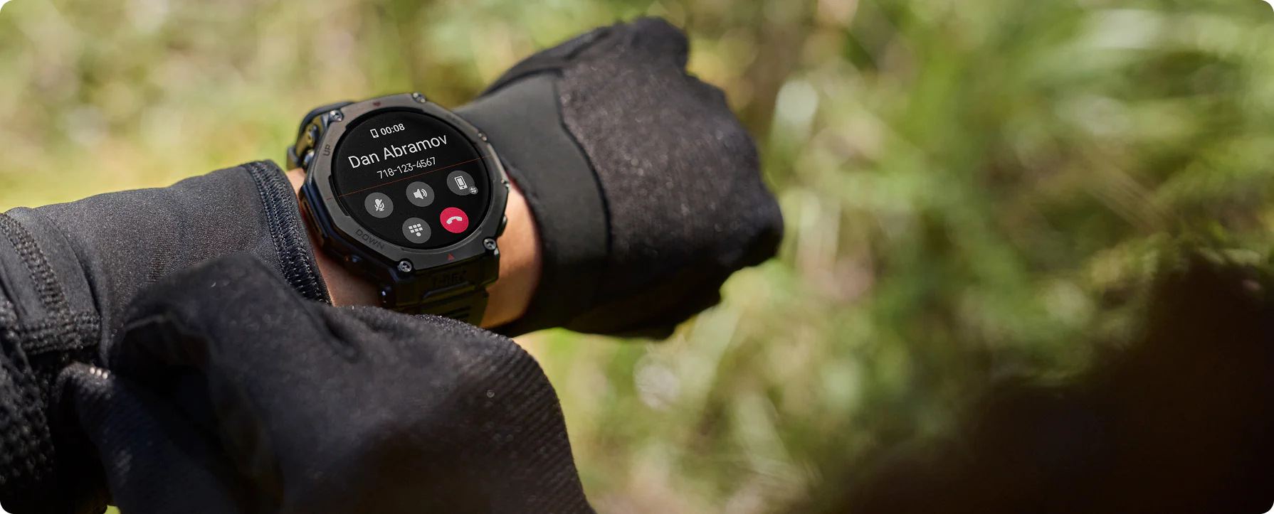 Une montre intelligente affiche un appel entrant de Dan Abramov. La montre est au poignet avec des gants noirs. Feuillage vert en arrière-plan.