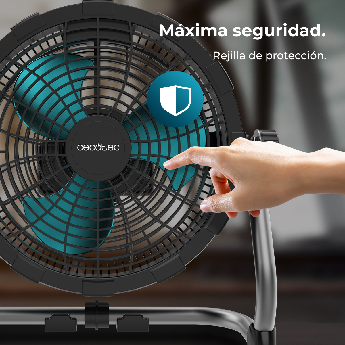 Una mano señala un ventilador. El ventilador es negro con aspas turquesas, un icono de escudo de seguridad y el texto 'Máxima seguridad'.