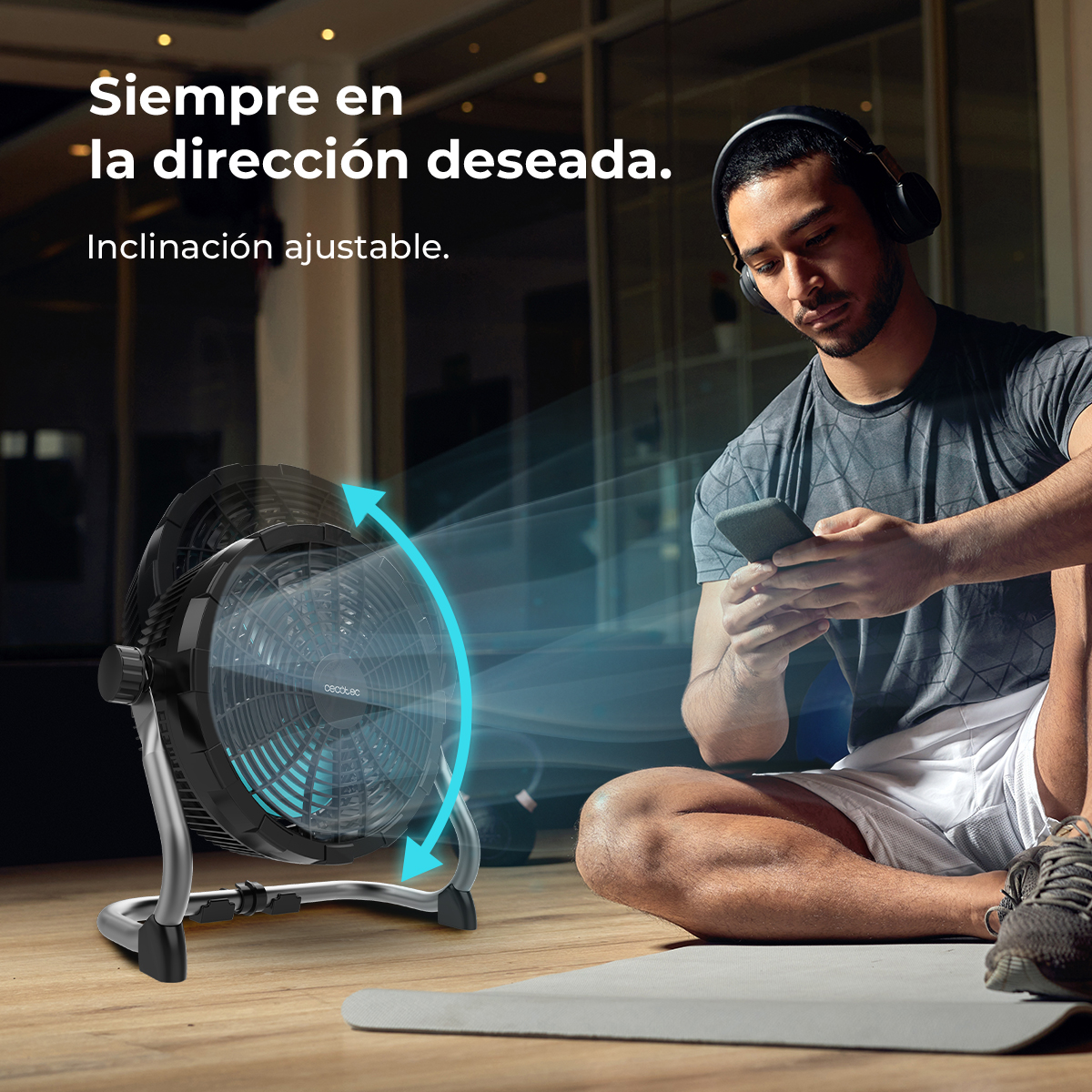 Hombre con auriculares usa un teléfono, un ventilador negro sopla aire. Texto: 'Siempre en la dirección deseada'.